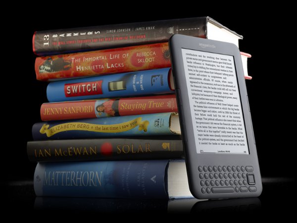 An electronic reader beside a stack of printed books