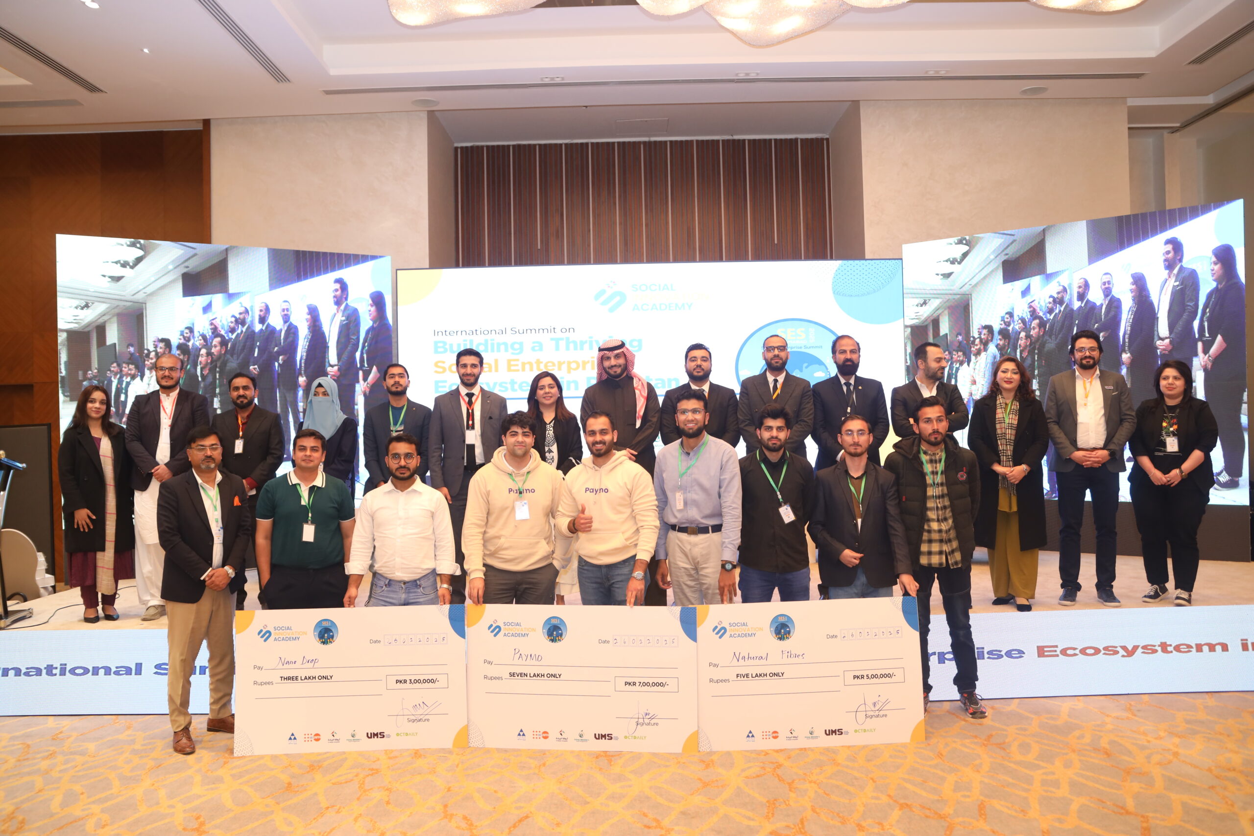 Participants at SIA's 2025 Social Enterprise Summit pose on stage behind three large award cheques