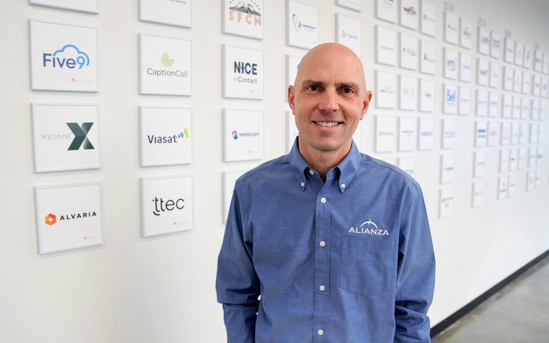 Alianza founder and CEO Brian Beutler standing before a wall of framed company logos