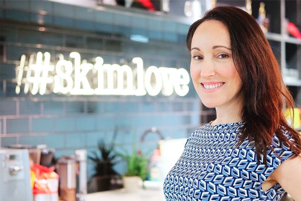Alicia Navarro beside the glowing #skimlove sign in the Skimlinks office