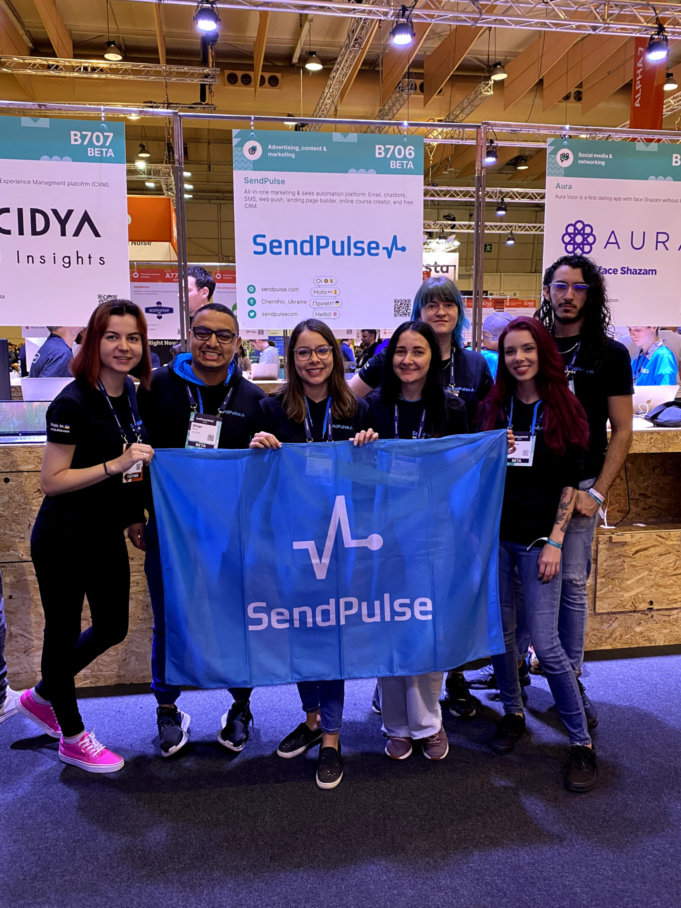 Alina Dykuha and the international SendPulse team holding a SendPulse flag at their Web Summit 2022 stand