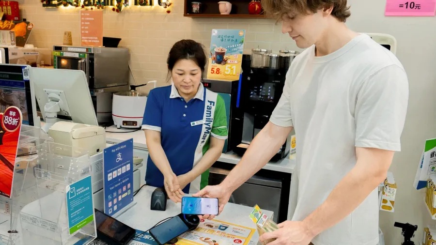 A FamilyMart customer holds an unlocked phone near an Alipay Tap terminal while buying a drink
