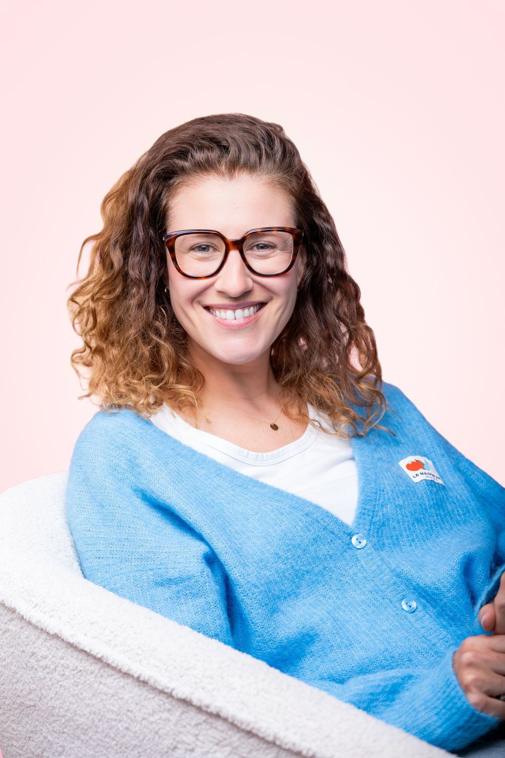Alix Coucardon seated against a pale pink backdrop, smiling in a blue cardigan