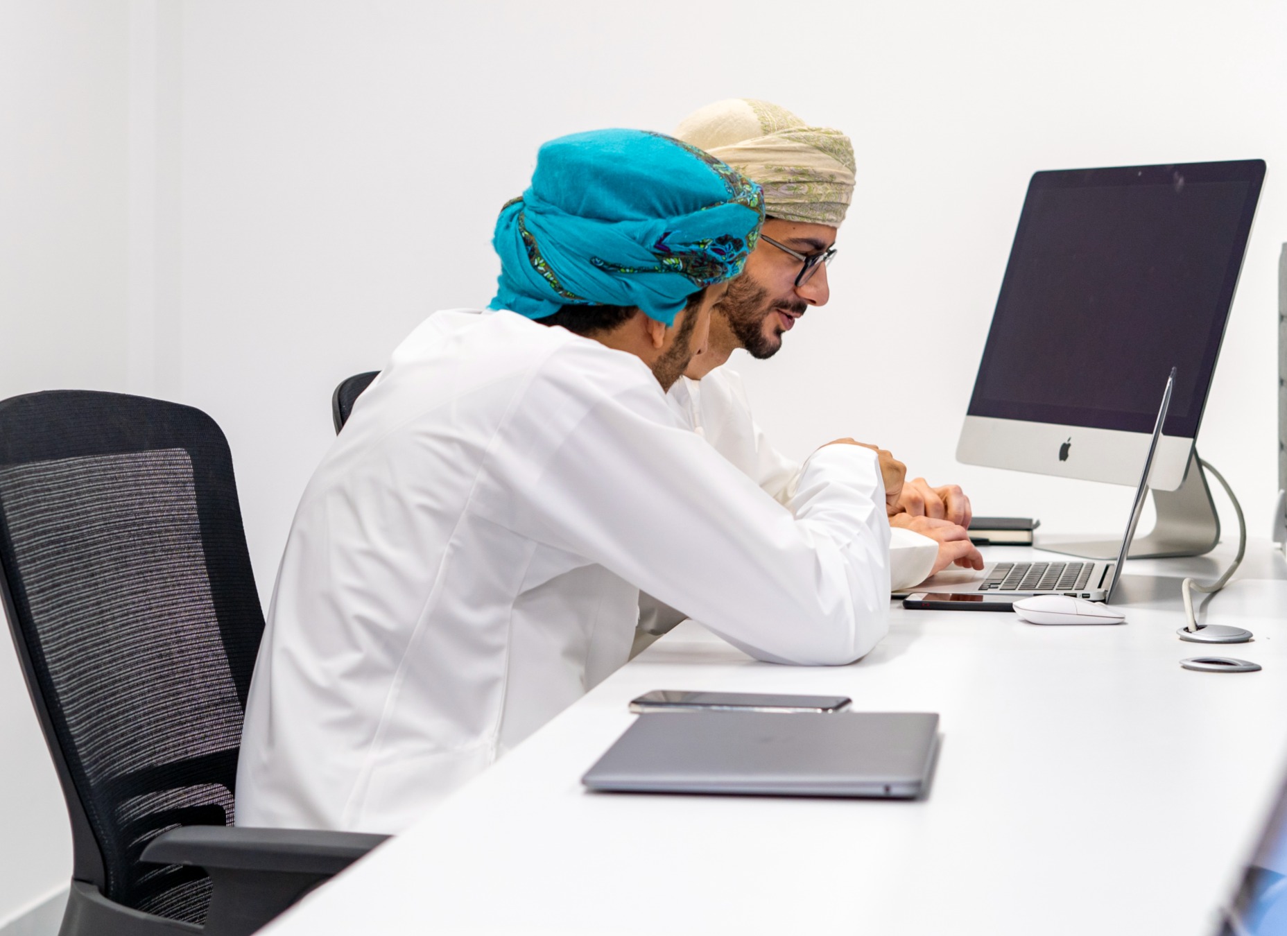 Two people collaborating at a desk with a laptop and desktop computer