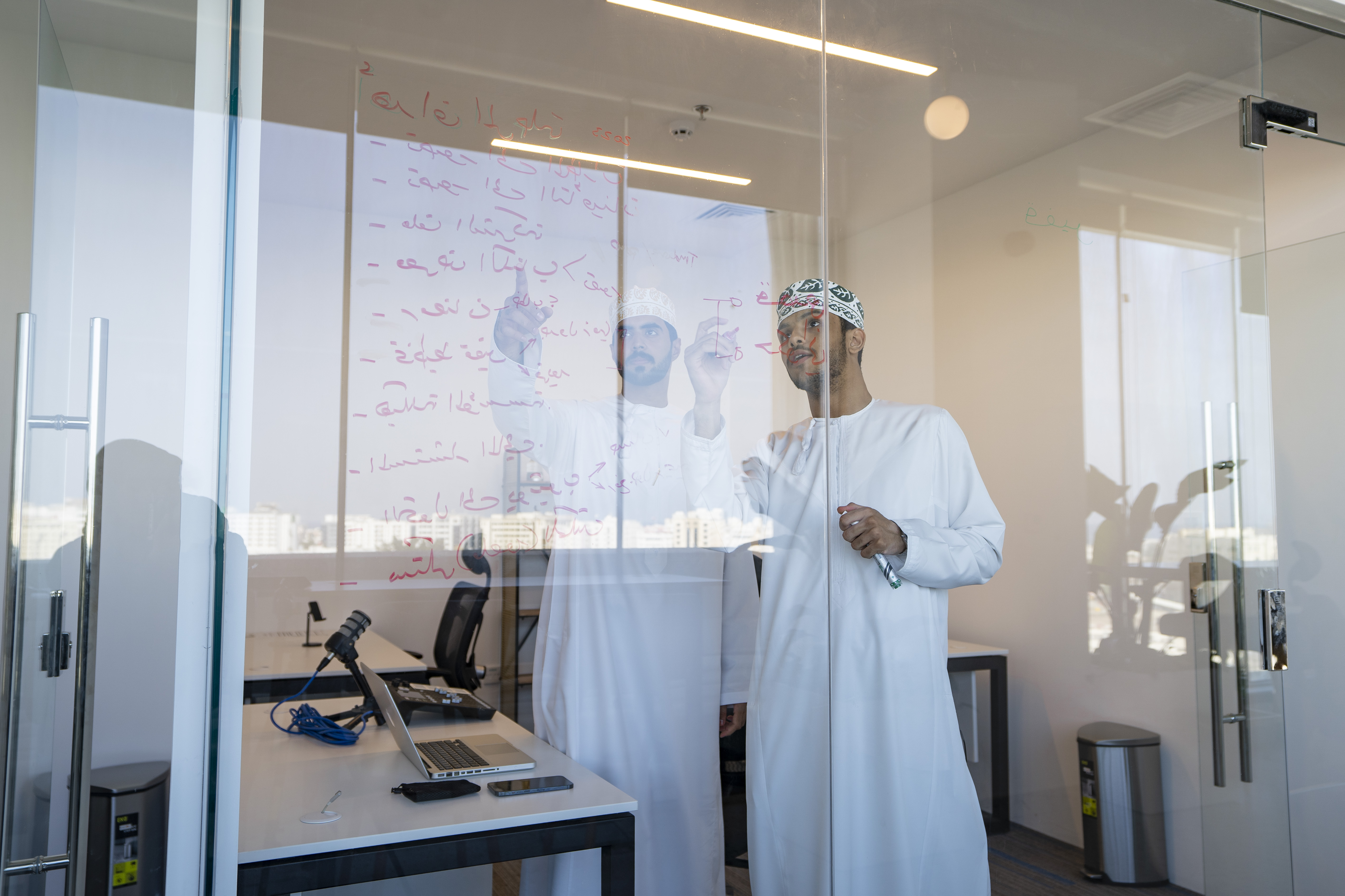 Two people working through notes written on a glass wall