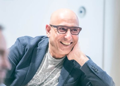 Alkarim Jivraj smiling in conversation, wearing glasses and a navy jacket