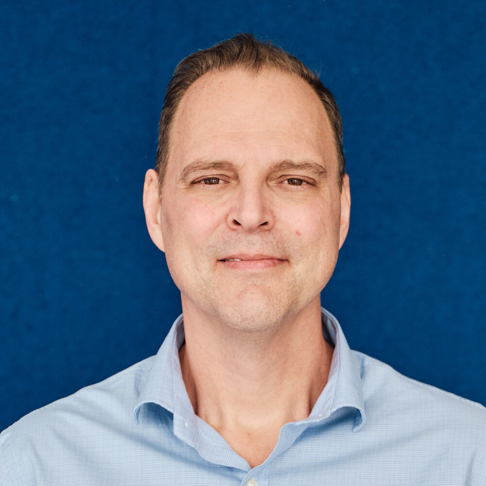 Allan Malcolm in a blue shirt against a blue studio background