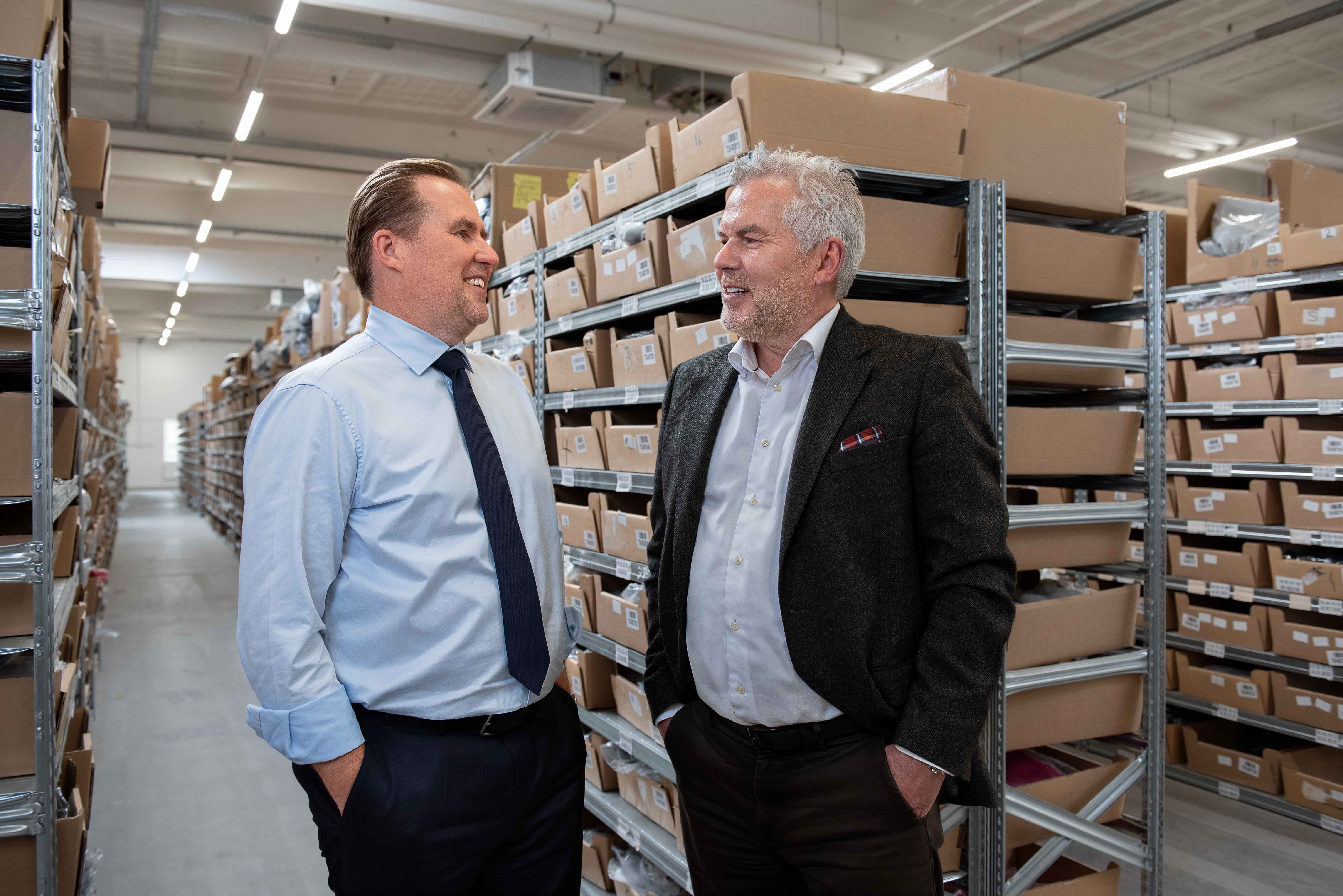 Allan Melgaard, left, and Jørgen Jessen talking between warehouse shelves
