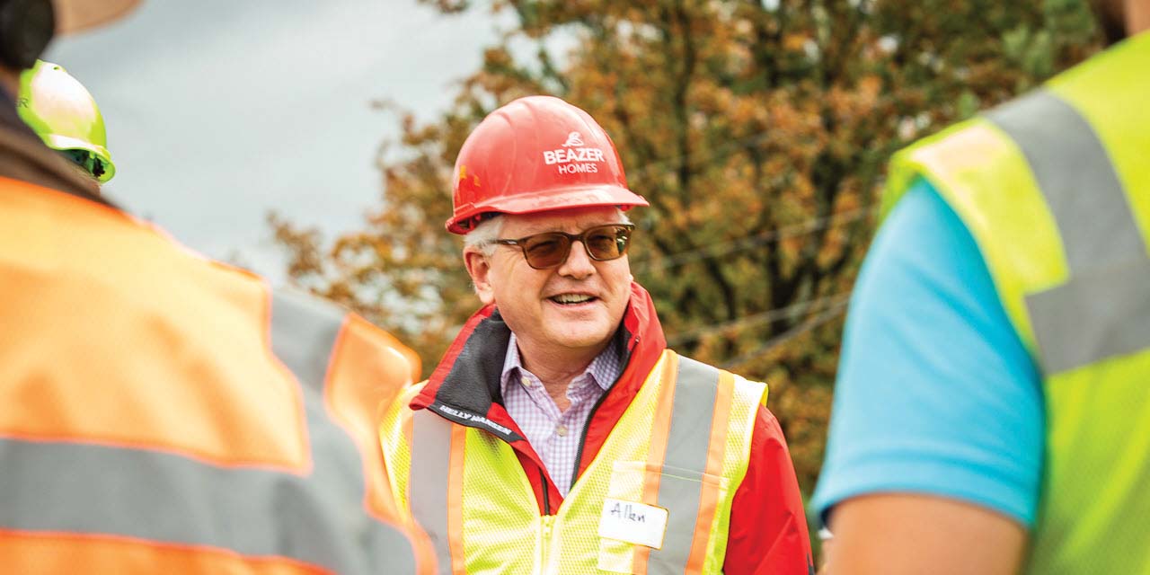 Allan Merrill in a red Beazer Homes hard hat, talking with people wearing safety vests