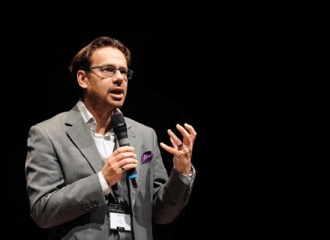 Allan Presland speaking onstage with a handheld microphone