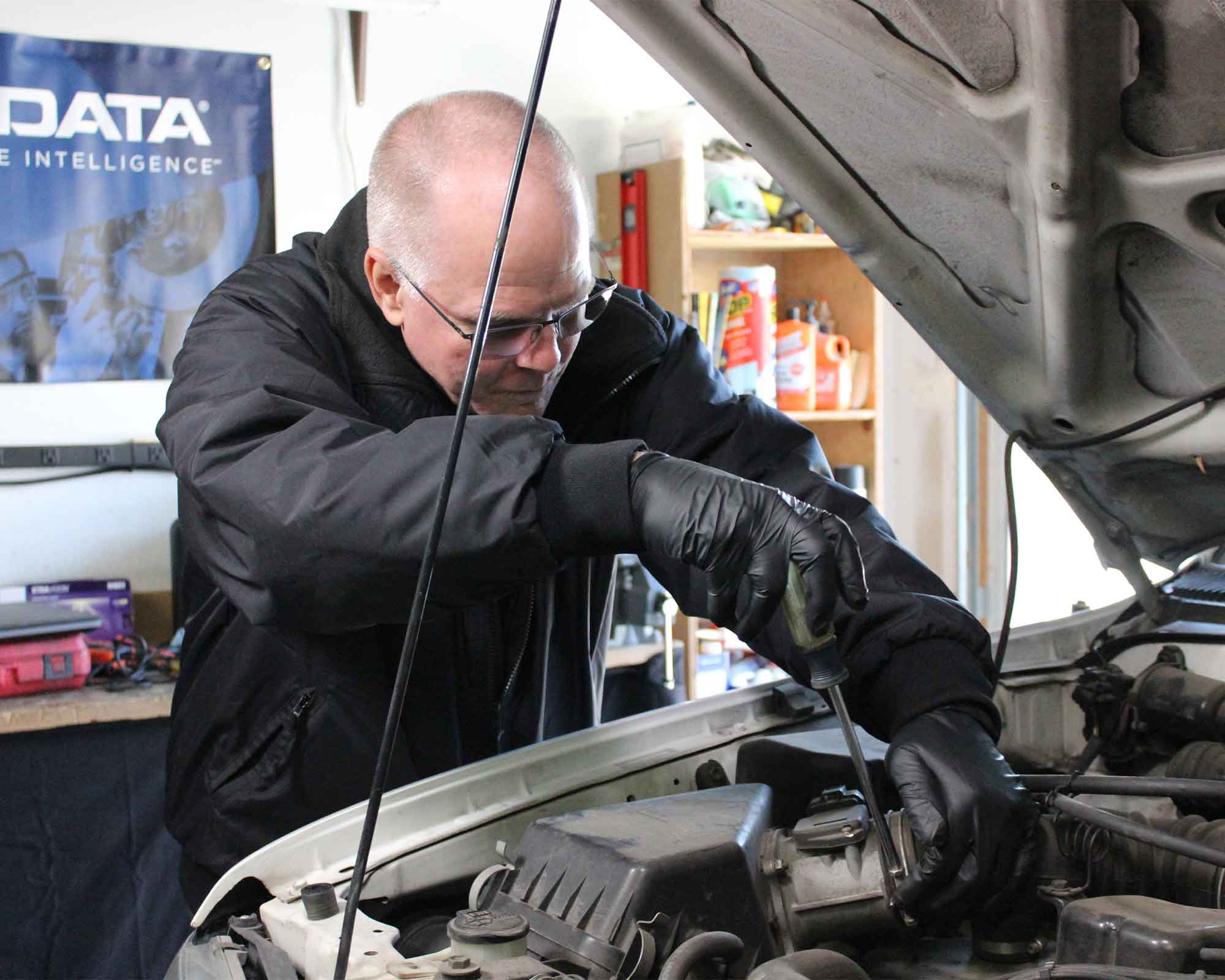 A technician working beneath an open car hood in an ALLDATA product photograph