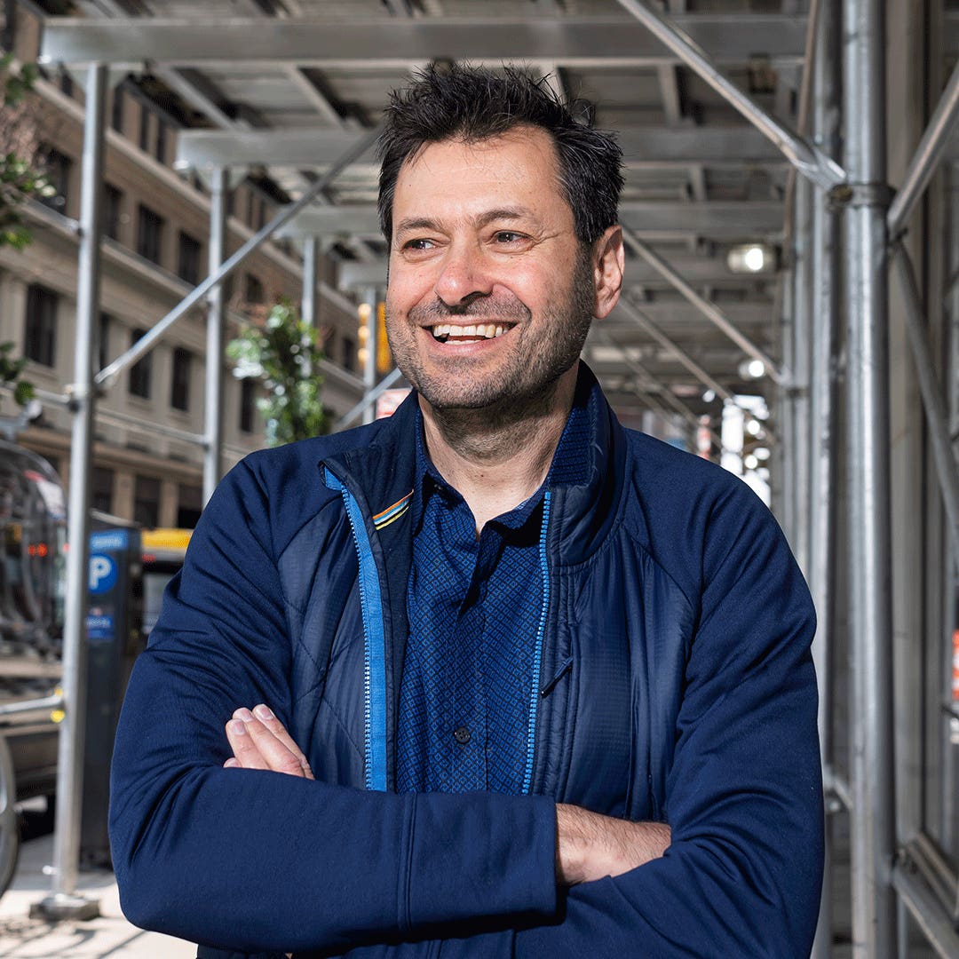 Allon Bloch smiling beneath scaffolding on a city sidewalk