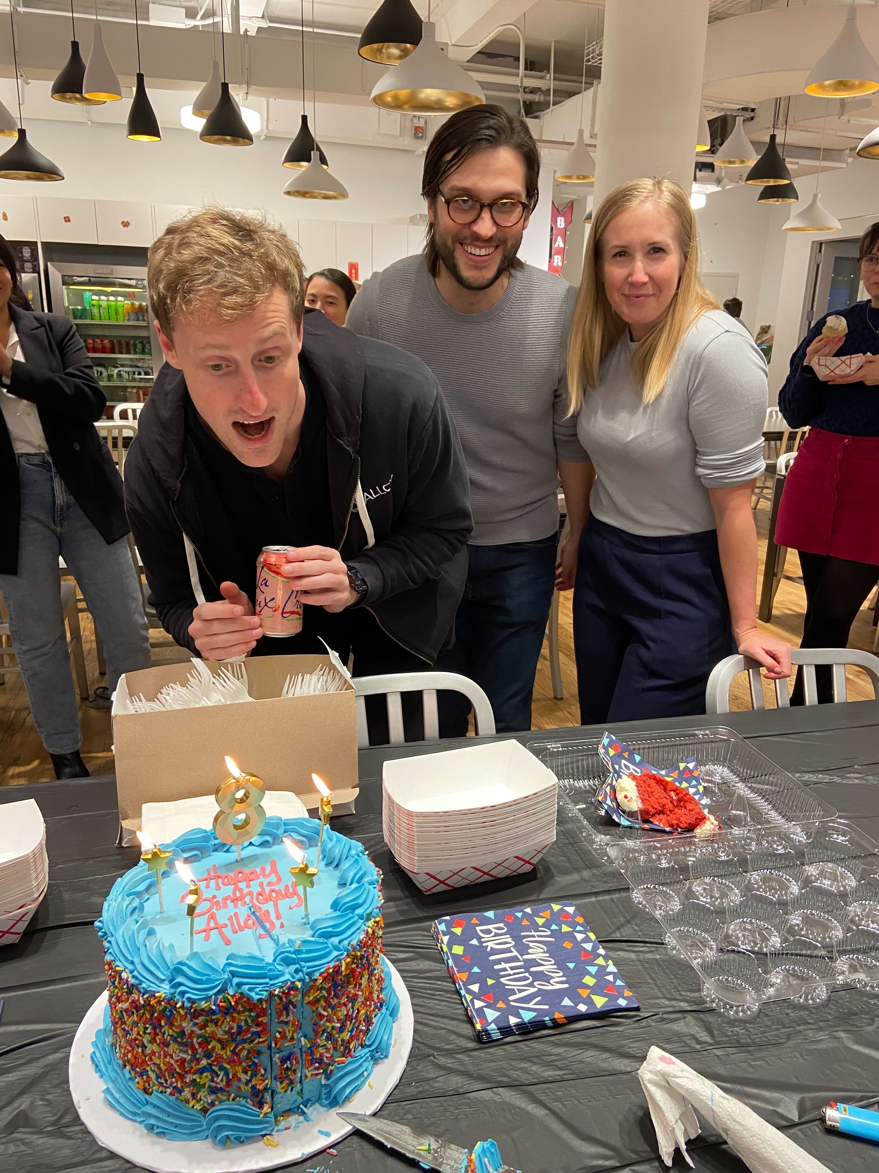 Alloy's founders and colleagues gathered around a blue eighth-birthday cake in the office