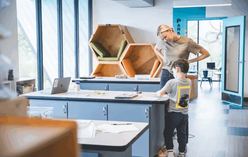 An Alpha guide stands beside a student working at a classroom table