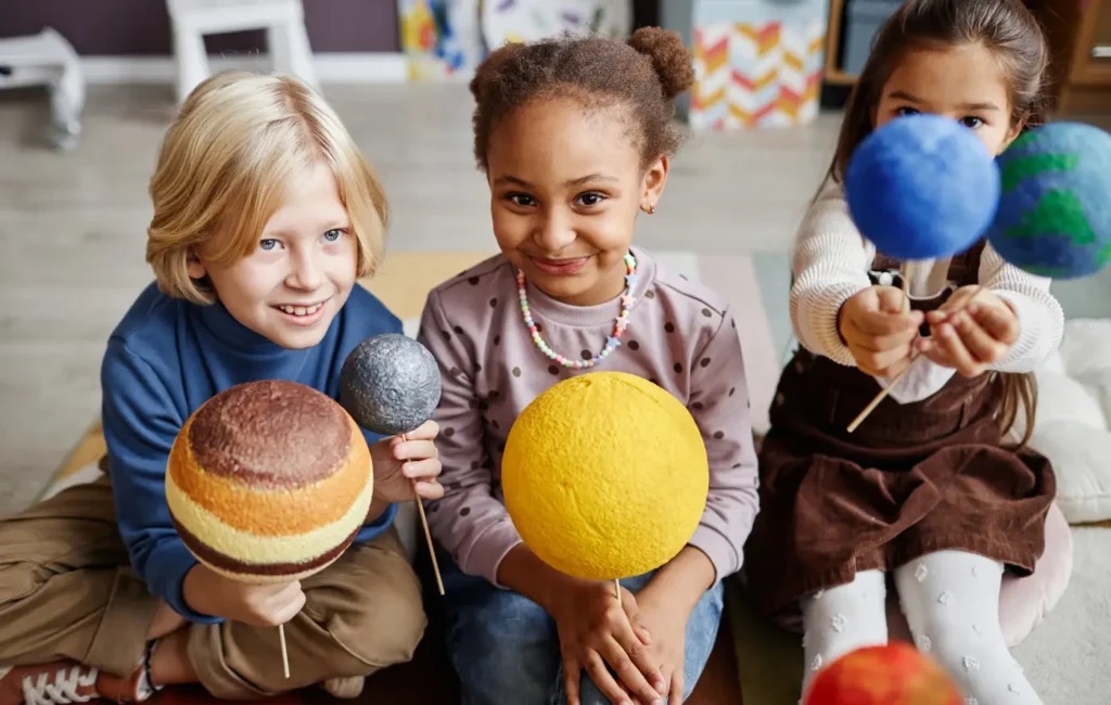Three students hold colorful models of planets