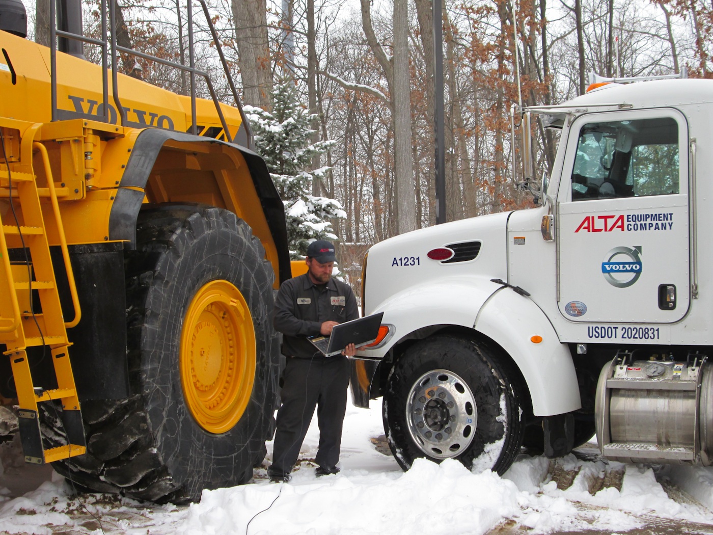 An Alta technician uses a laptop between a Volvo construction machine and an Alta service truck in the snow.