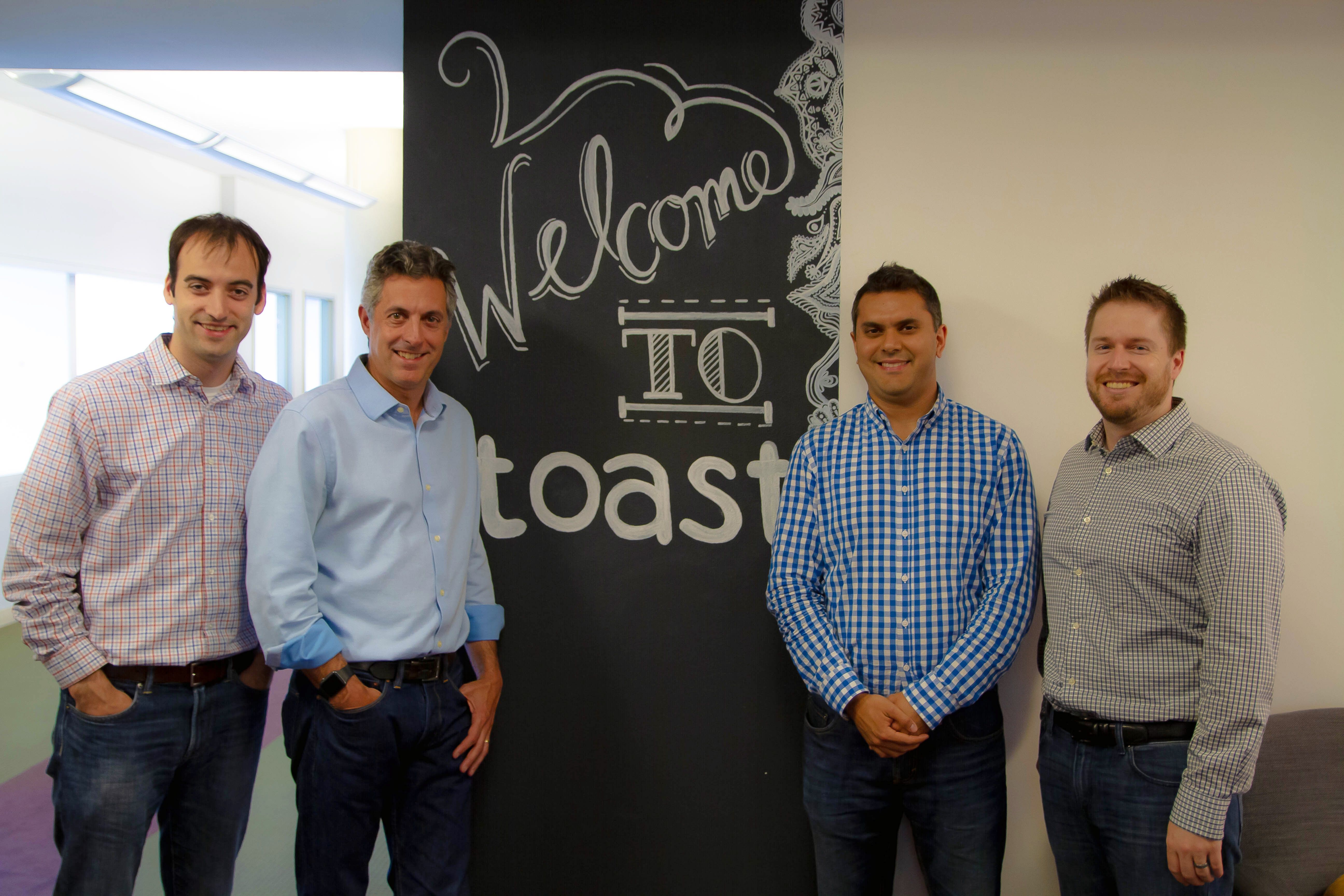 Toast leaders Steve Fredette, Chris Comparato, Aman Narang, and Jonathan Grimm standing together in front of a Welcome to Toast chalkboard