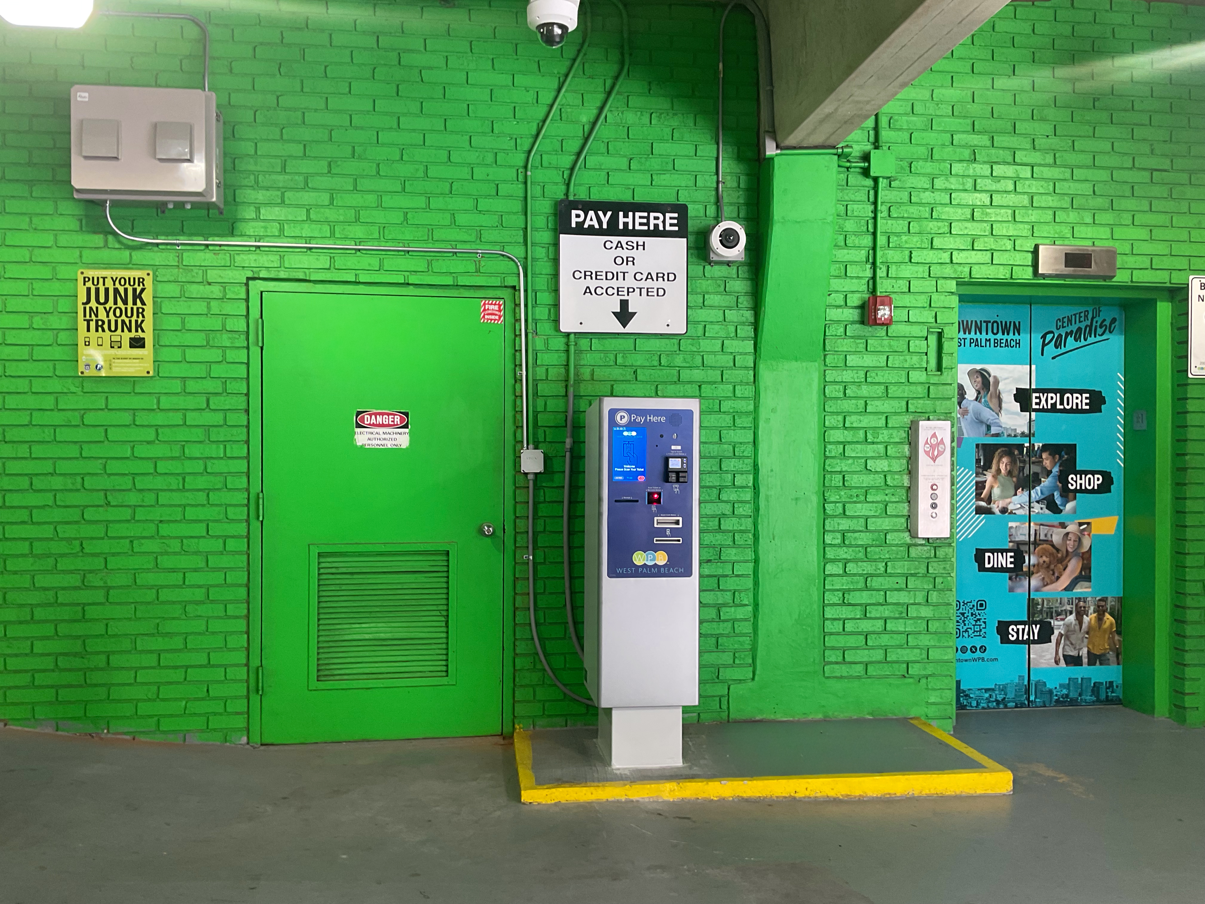 Amano ONE pay-on-foot kiosk against a green West Palm Beach garage wall, with cash and credit card signage