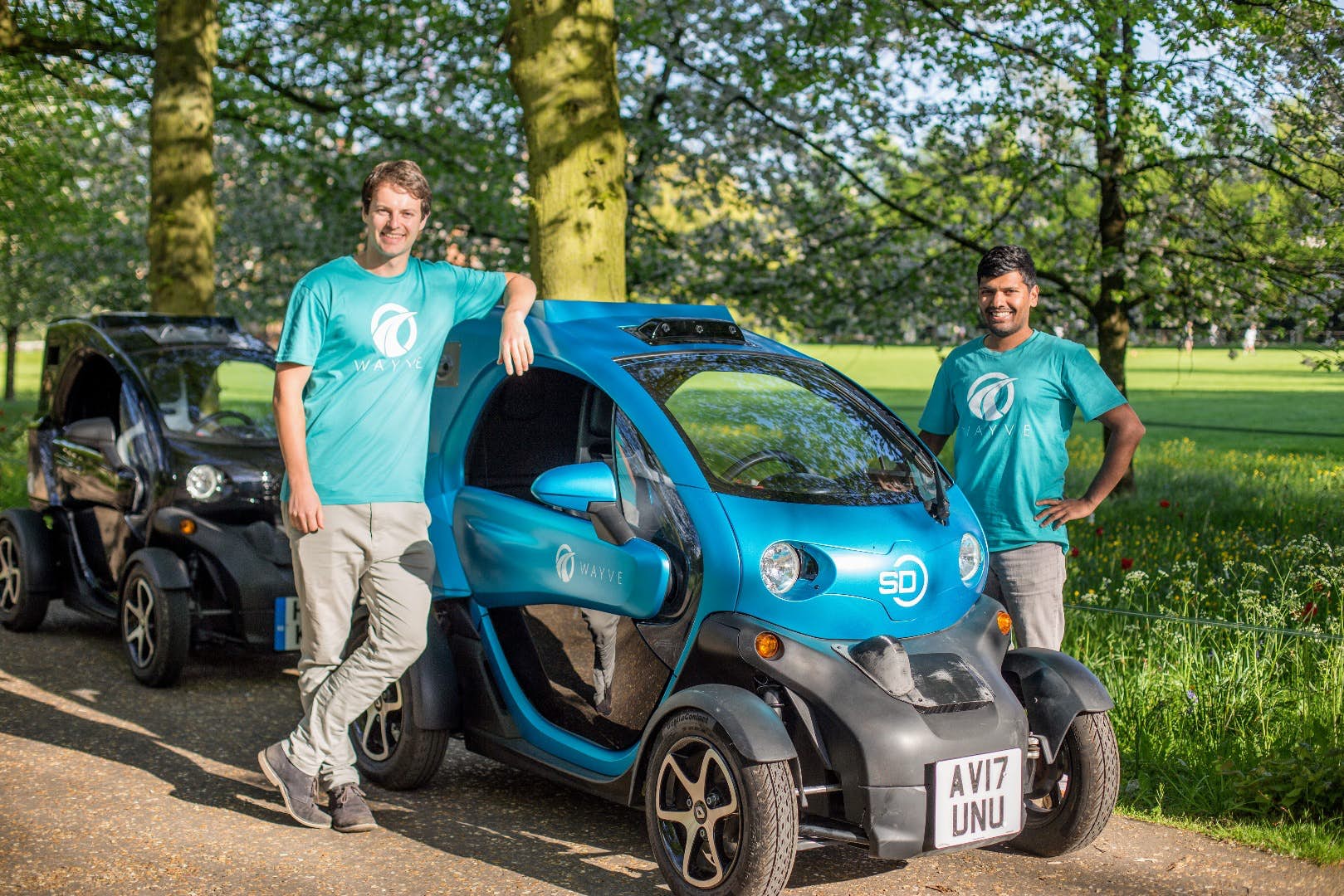 Alex Kendall on the left and Amar Shah on the right, standing beside an early blue Wayve vehicle