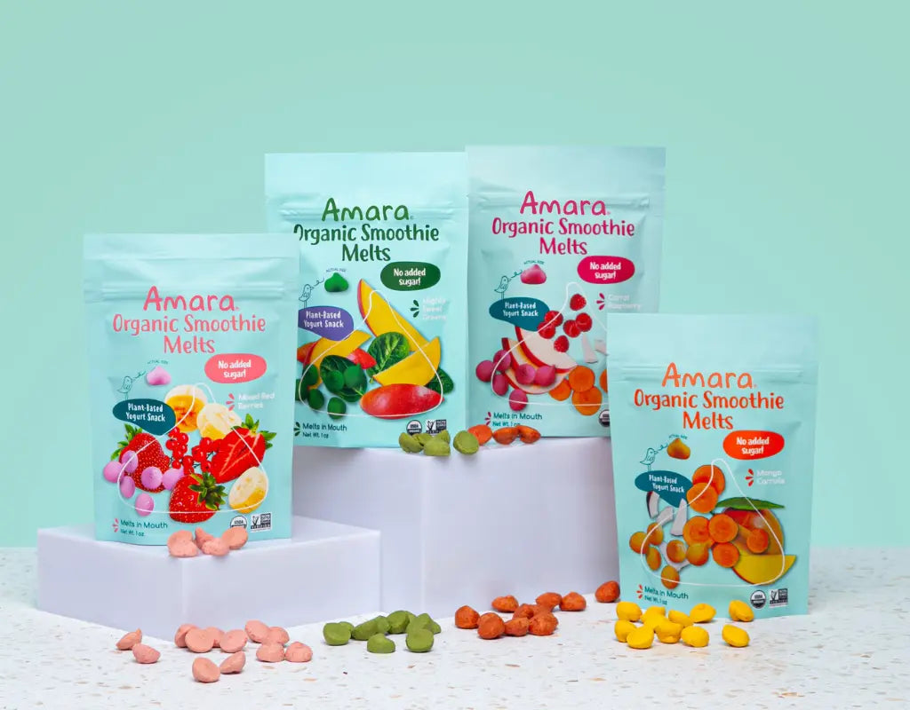 Four colorful pouches of Amara Organic Smoothie Melts surrounded by fruit and snack pieces