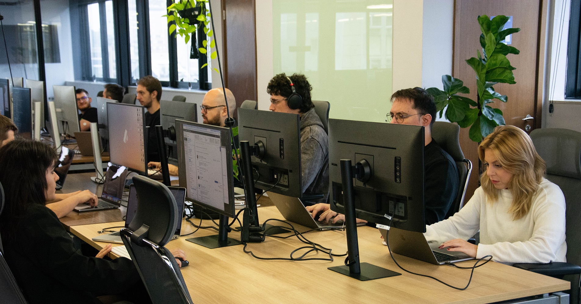 People working at a shared desk with laptops and large monitors, from Ambush’s careers page