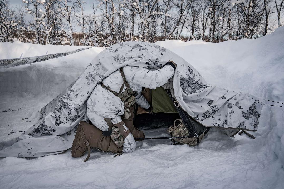 Snow-pattern clothing and a concealment hide in a wooded arctic setting