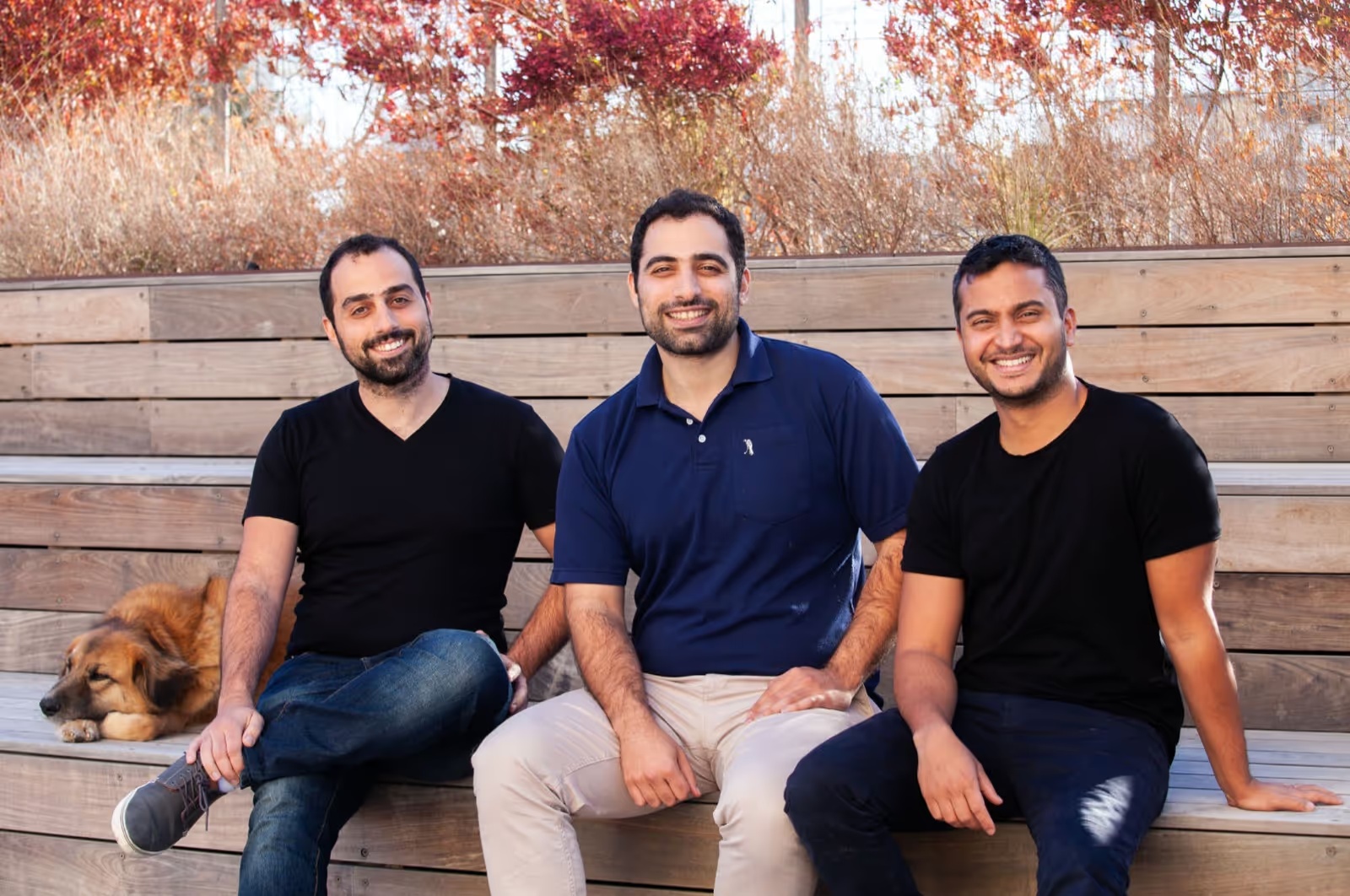 Connecteam’s three co-founders seated outdoors, with Amir Nehemia on the right and a dog resting beside them