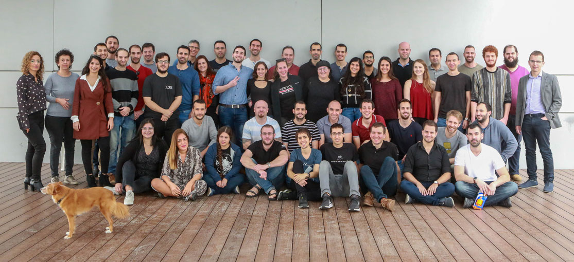 Claroty employees gathered for a team photograph on a wooden deck, with a dog in the foreground