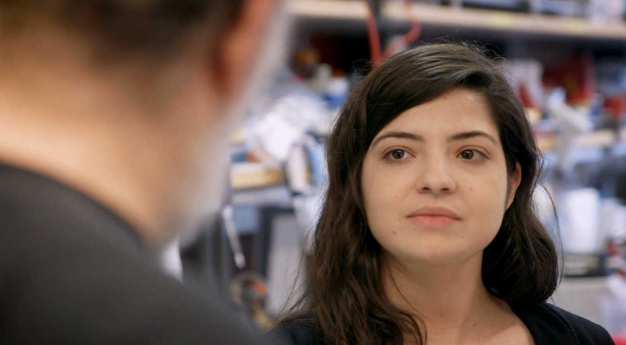 Amira Barkal in a Stanford laboratory, looking toward a colleague in the foreground