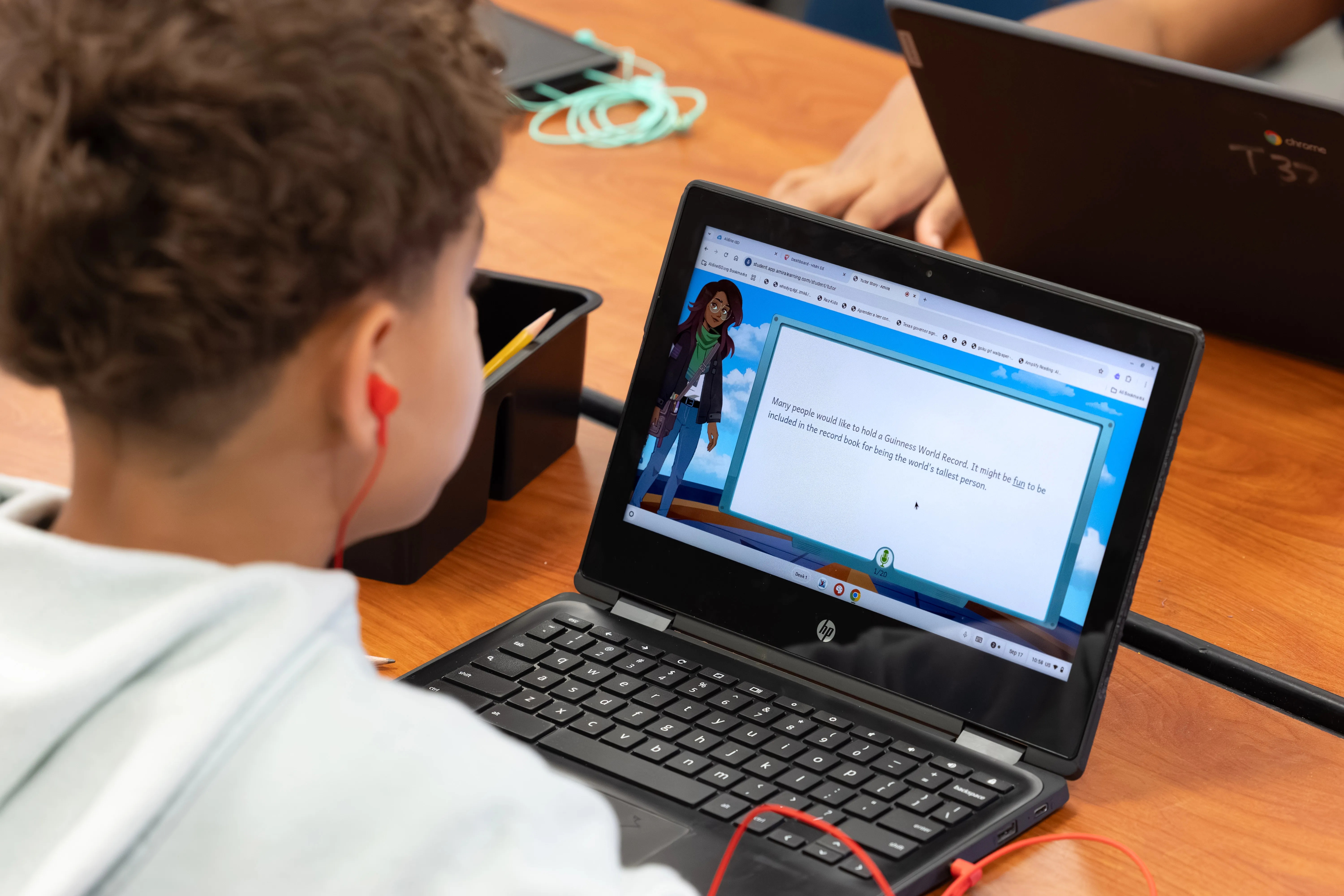 A student wearing earphones reads a passage on a laptop displaying the Amira reading assistant.