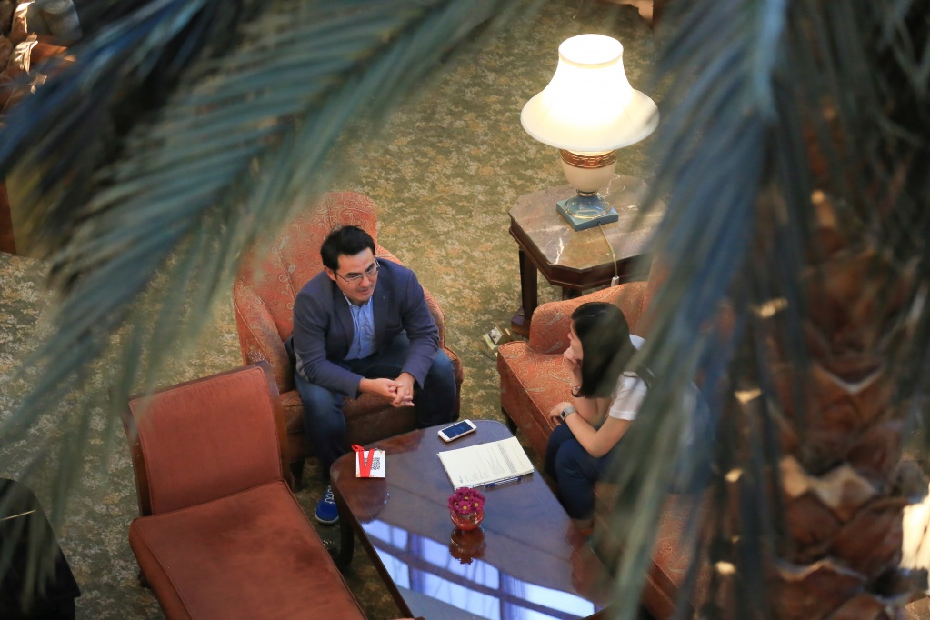 Amirkhan Omarov seated opposite an interviewer, seen from above through a staircase railing
