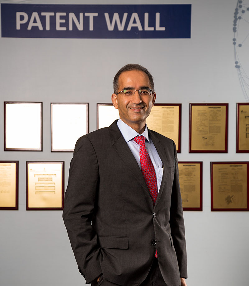 Amit Chadha standing beside a wall of framed patent documents