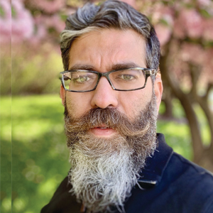 Amit Vohra outdoors, wearing glasses and a blue shirt