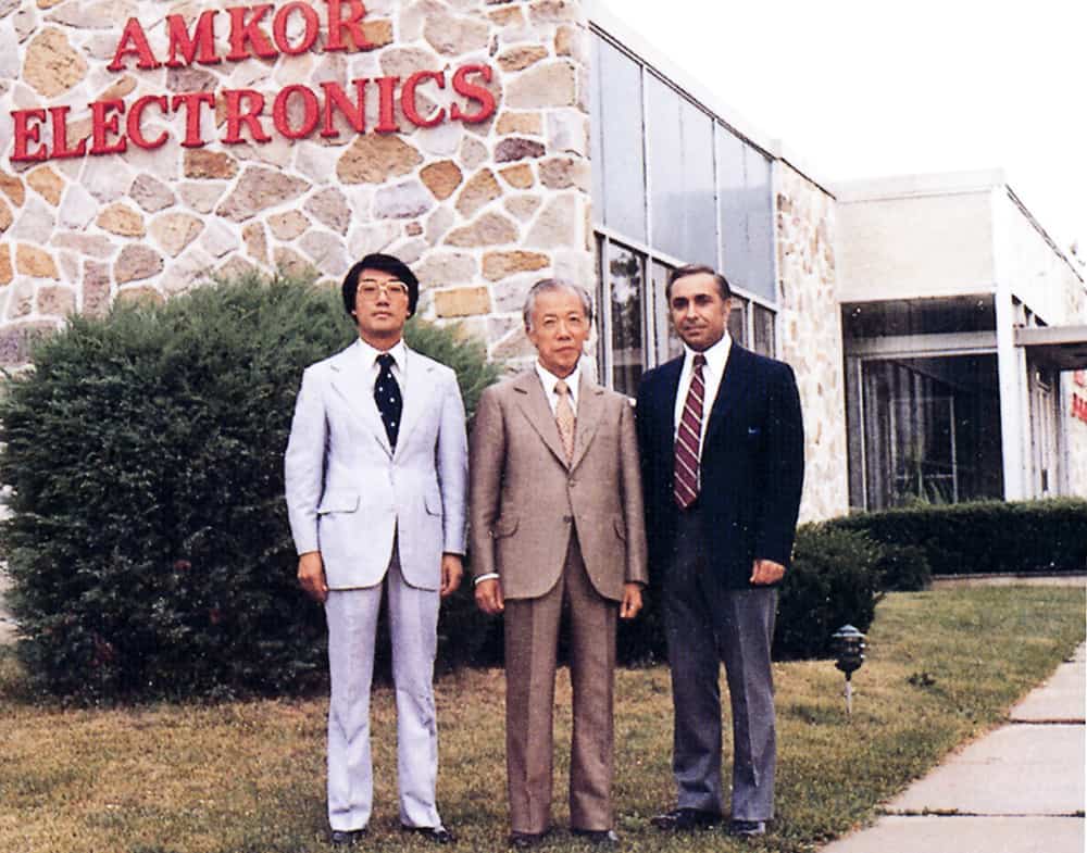 Archival photograph of three Amkor leaders outside an Amkor Electronics building