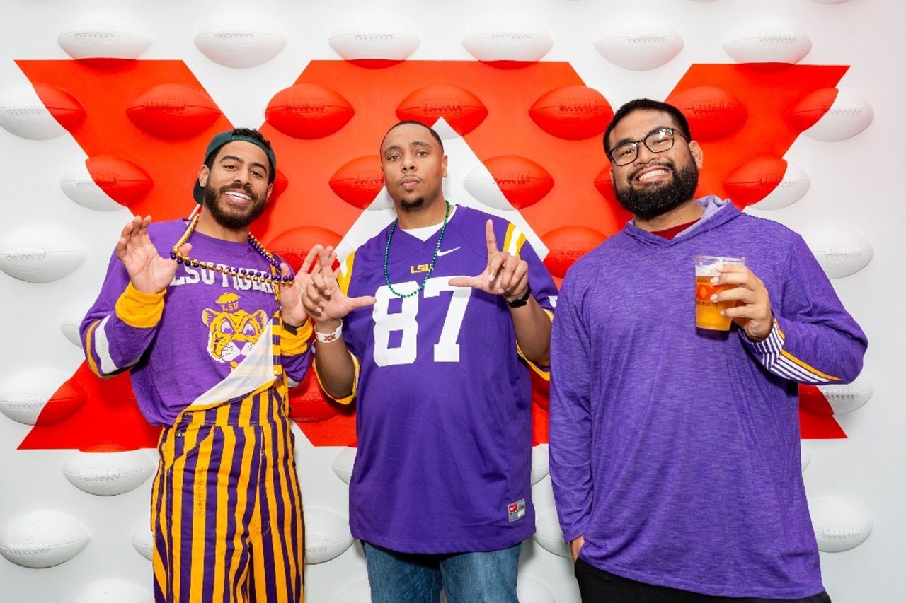College football fans pose in front of a red Dos Equis football wall at a brand activation