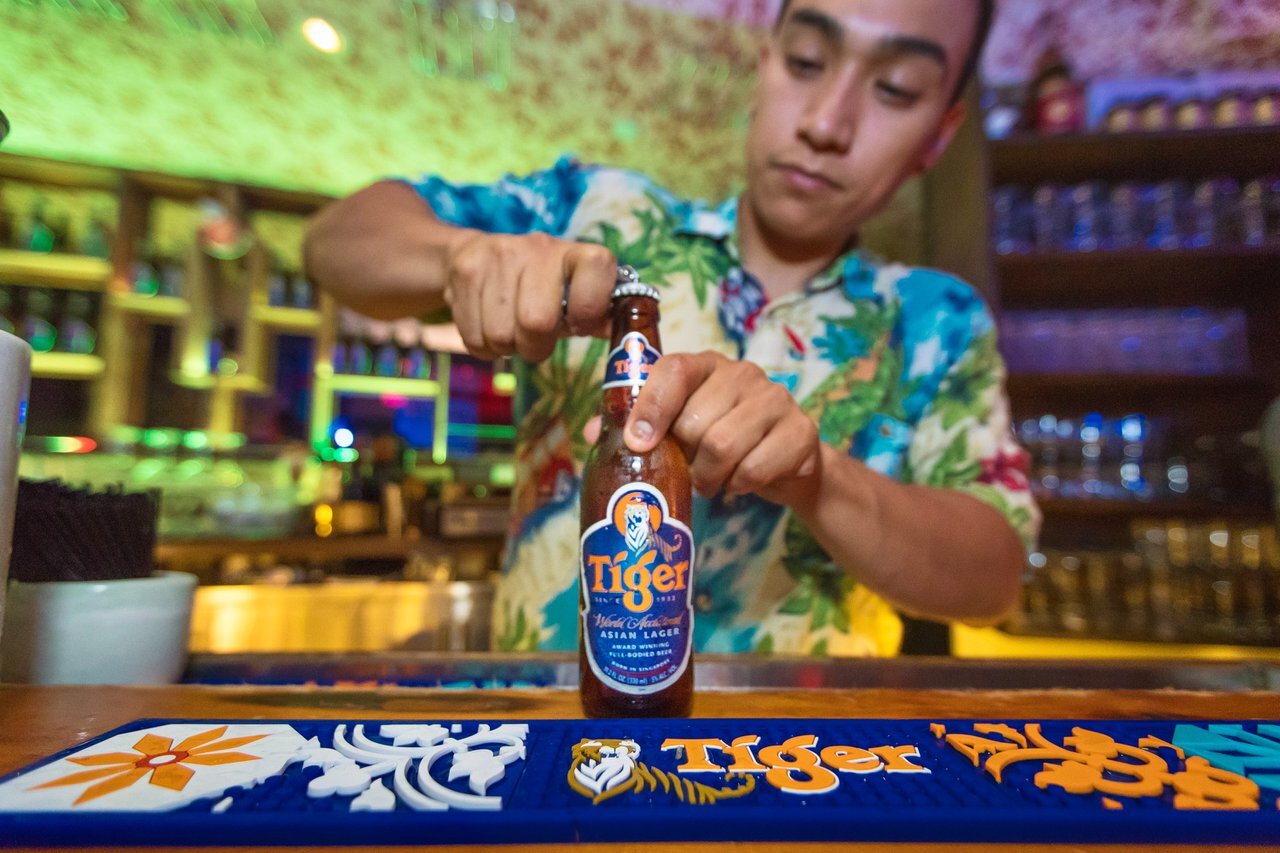 A bartender opens a Tiger Beer bottle at a colorful event bar
