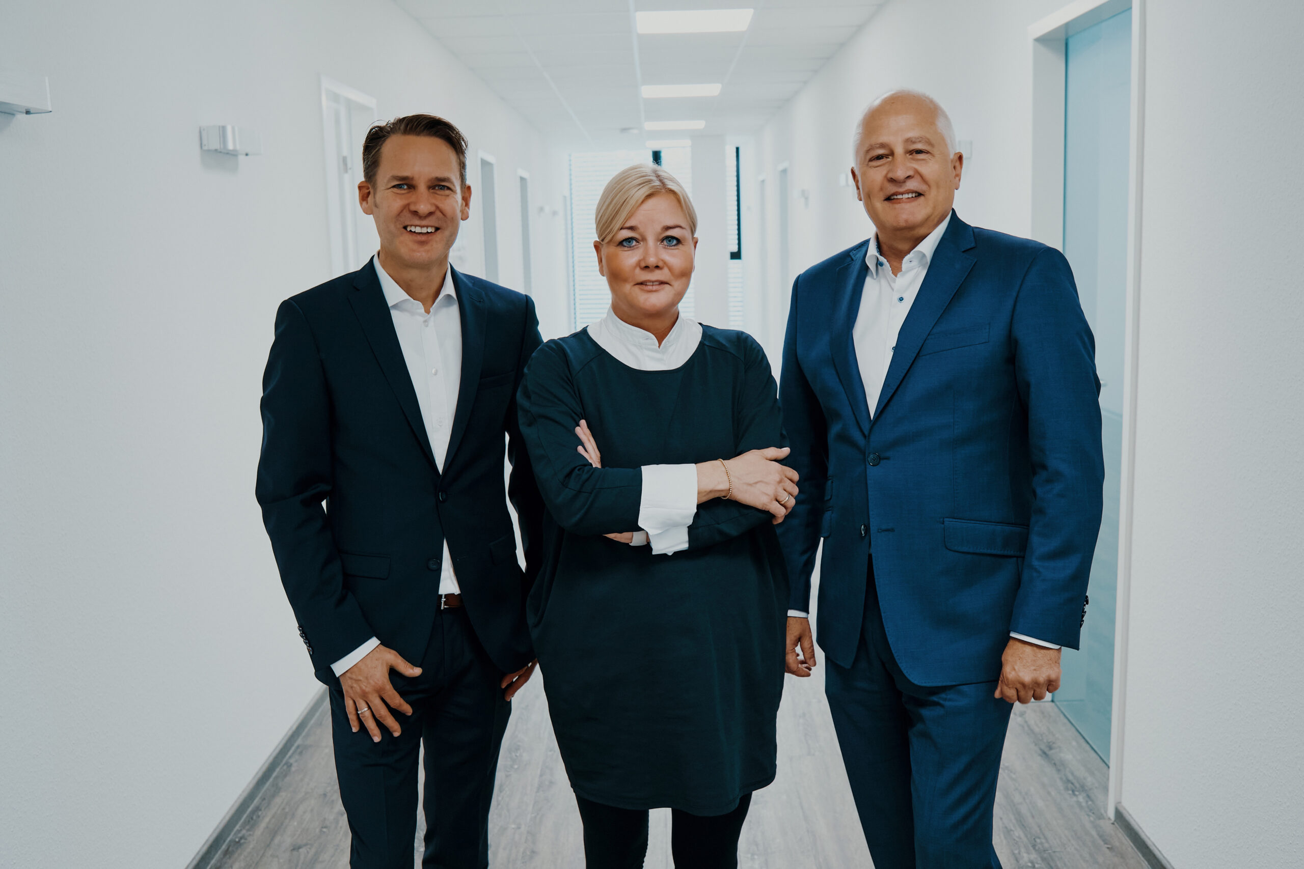 Three ams board members standing together in an office corridor, with Simone Schiffgens in the center