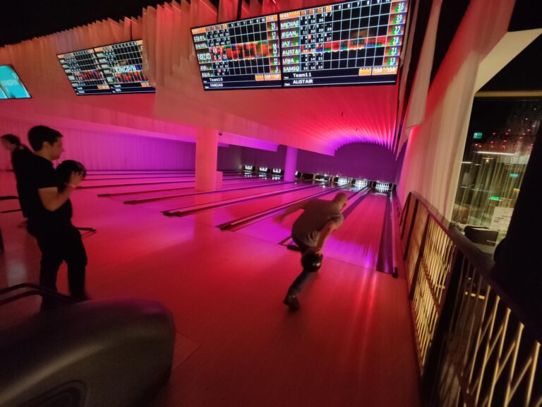 People bowling beneath illuminated scoreboards in Amused Group’s culture gallery