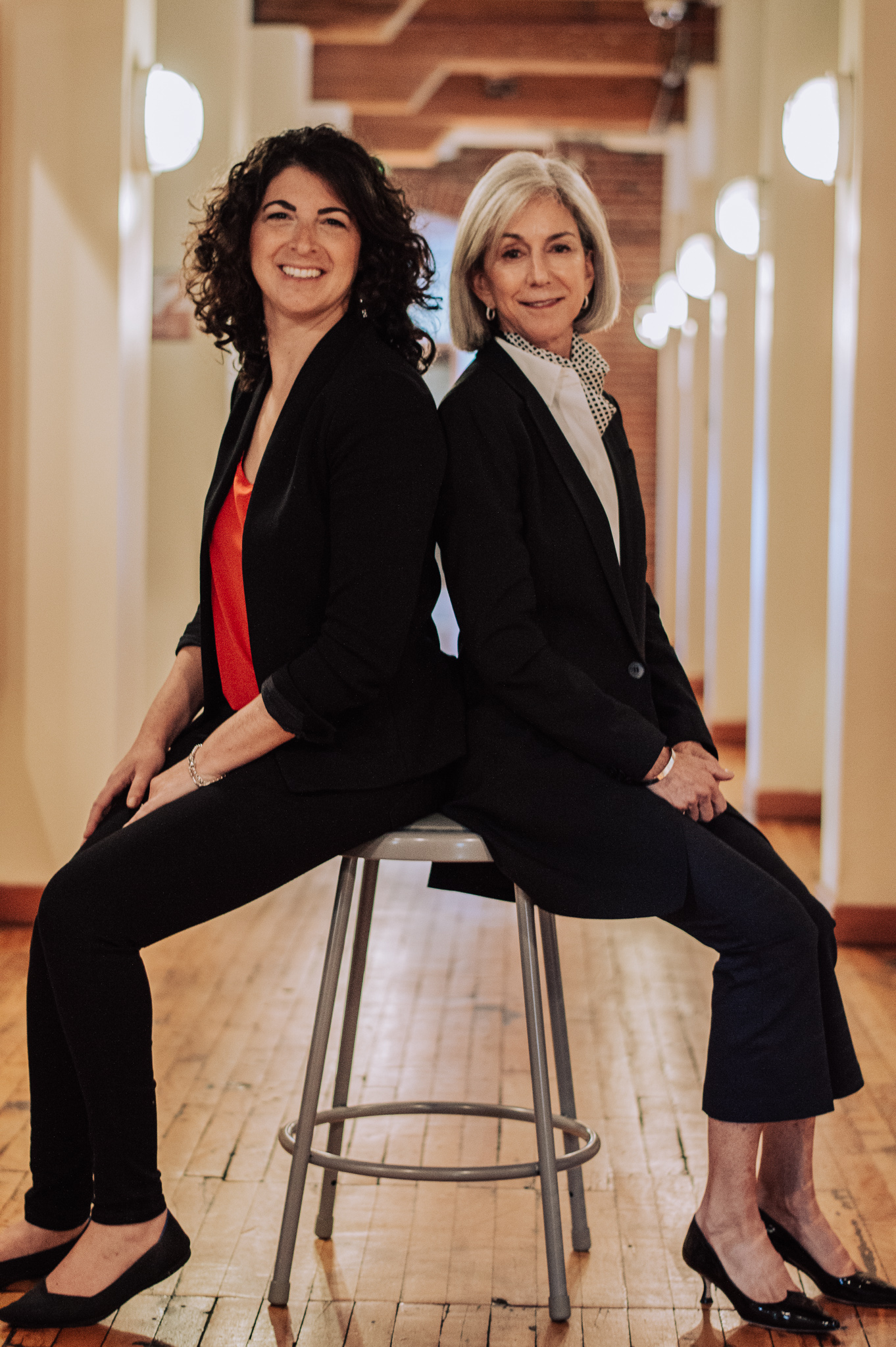 Amy Burke Friedman, left, and Amy Elias, right, seated together in a bright hallway