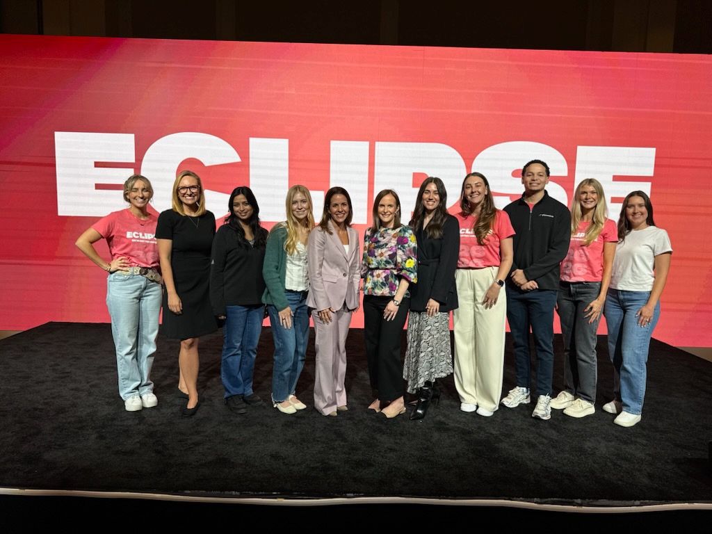 Ana Perez, centered in a pale suit, standing with the PlanSource team in front of an Eclipse event screen
