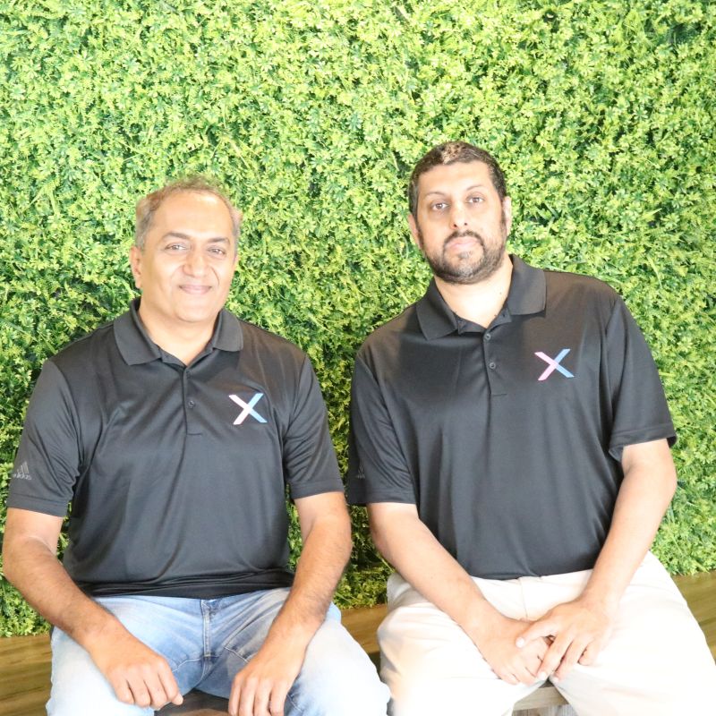 Anand Nagaraj, left, and Ahmad Malik in black CredibleX polo shirts in front of a green wall