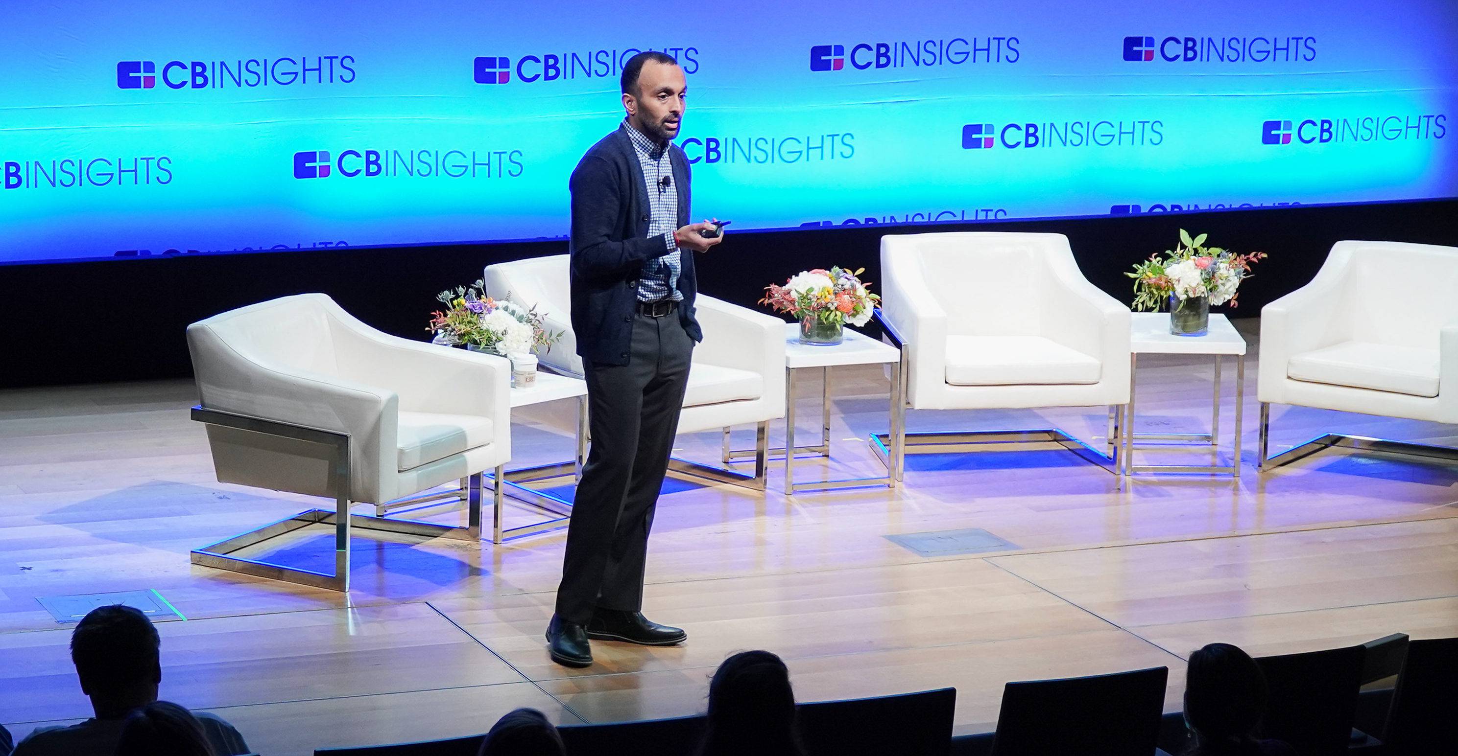 Anand Sanwal speaking onstage at a CB Insights conference, holding a presentation remote.