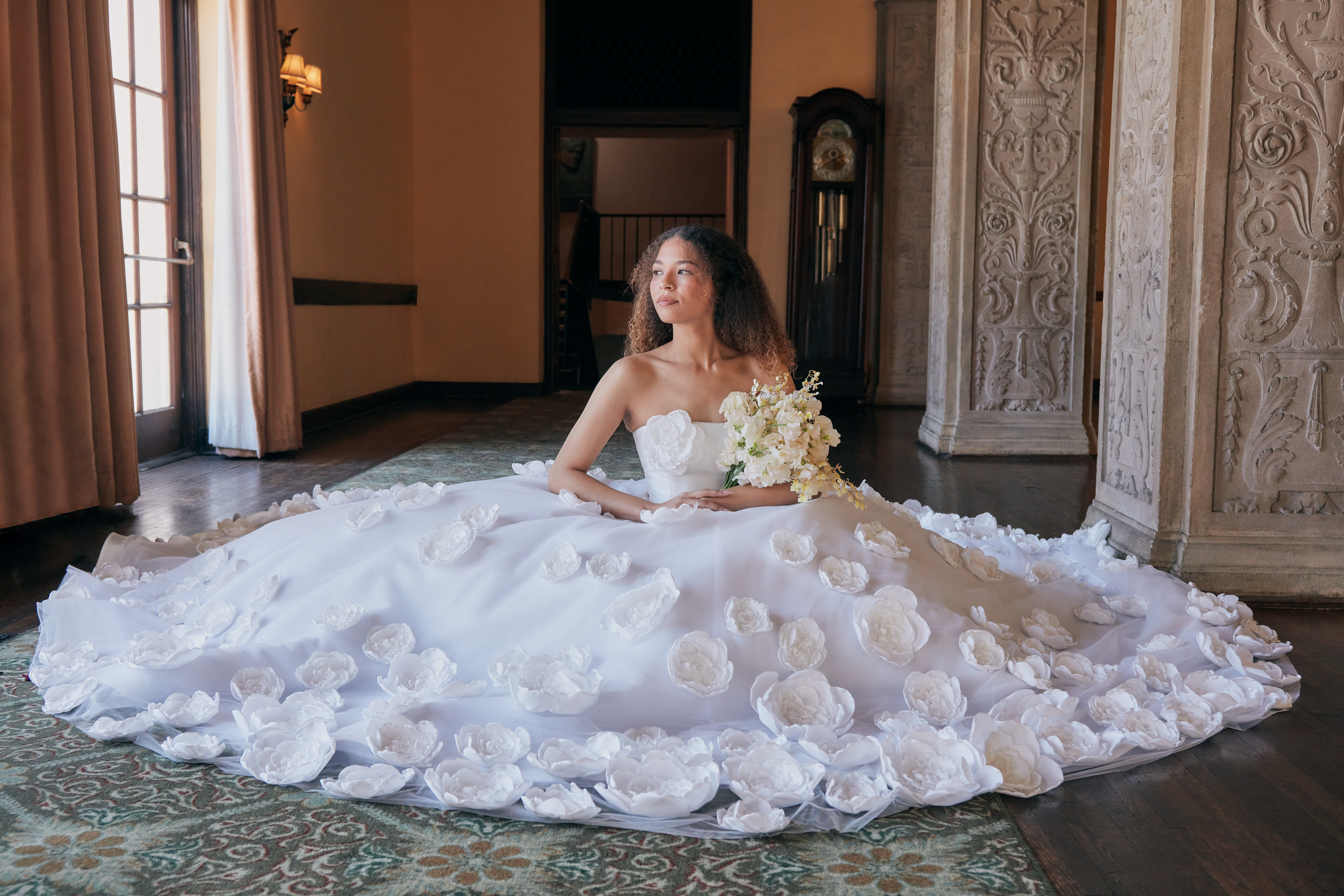 A model in a flower-covered white bridal gown seated inside The Ebell of Los Angeles