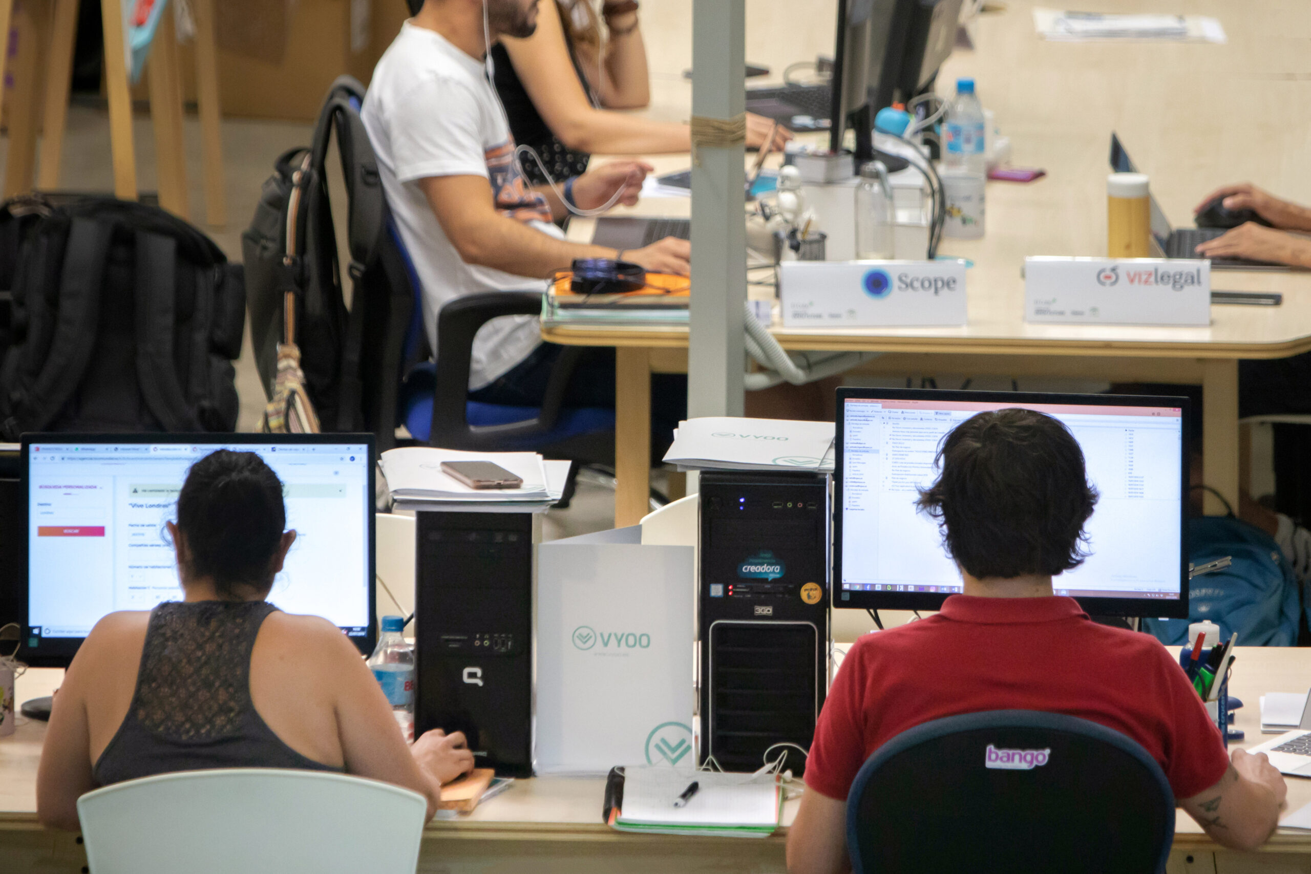 Entrepreneurs at shared desks inside El Cubo, with monitors and startup name cards