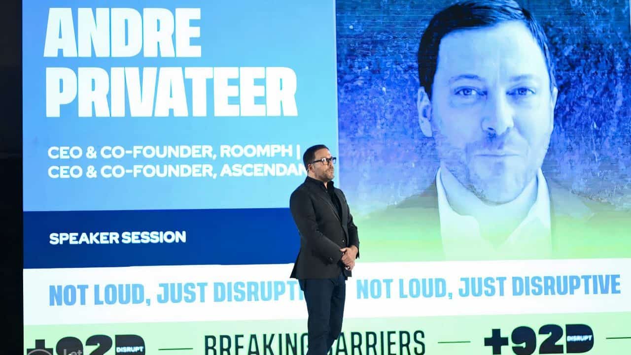 Andre Privateer speaking onstage at +92Disrupt, with his name projected behind him