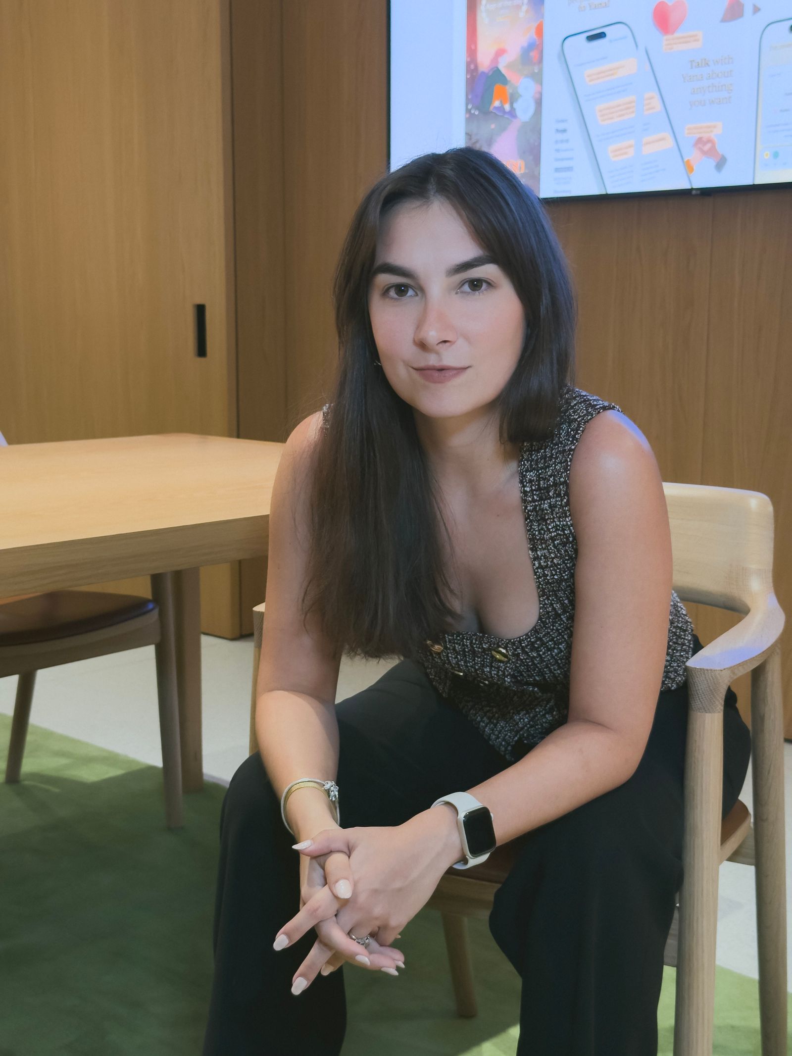 Andrea Campos seated in a modern meeting room with Yana app screens visible behind her
