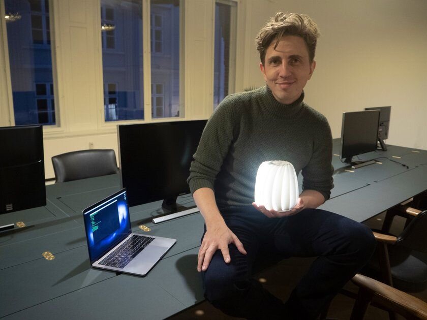 Andreas Cleve seated at a worktable beside a laptop and holding a glowing lamp