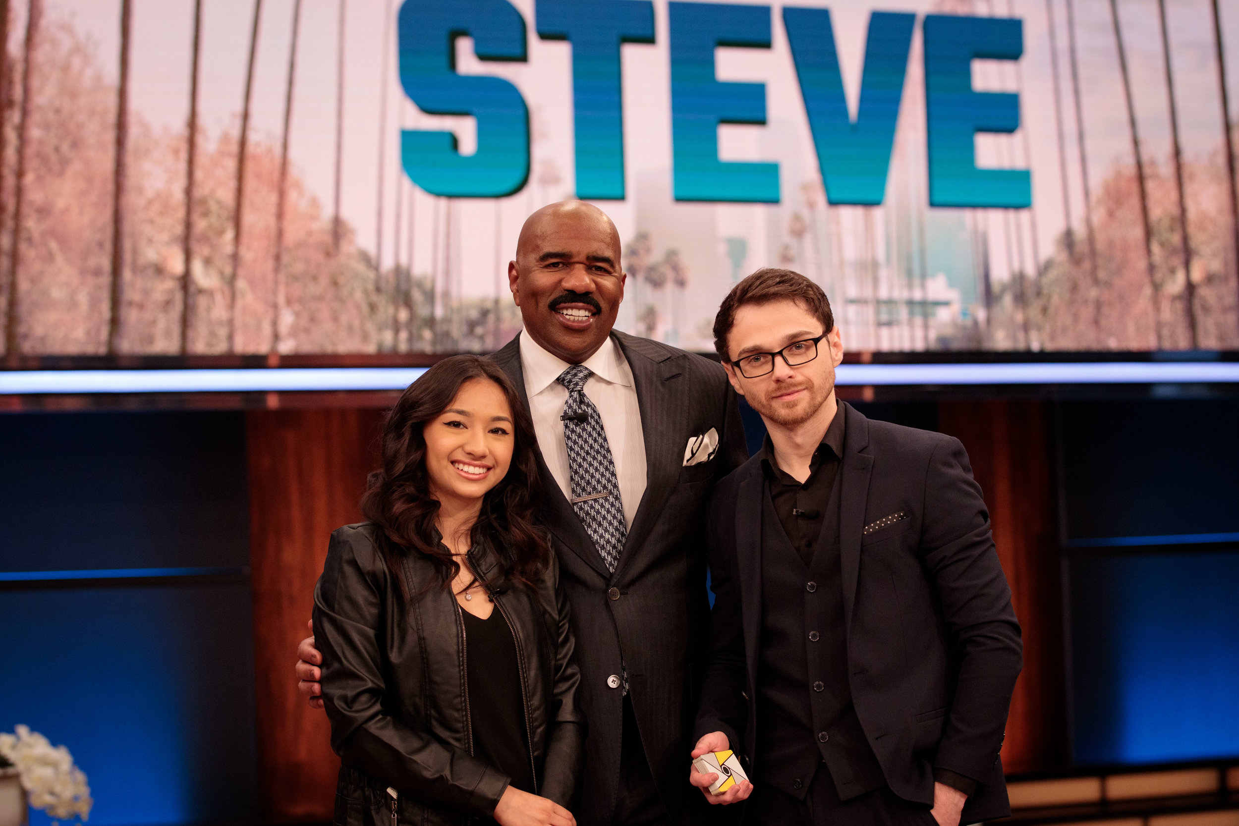 Andrei Jikh with Steve Harvey and a fellow performer on a television set