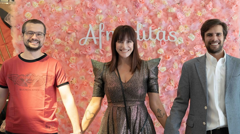 Jorge López, Connie Ansaldi and Andrés Lawson stand together in front of a pink floral Afroditas backdrop