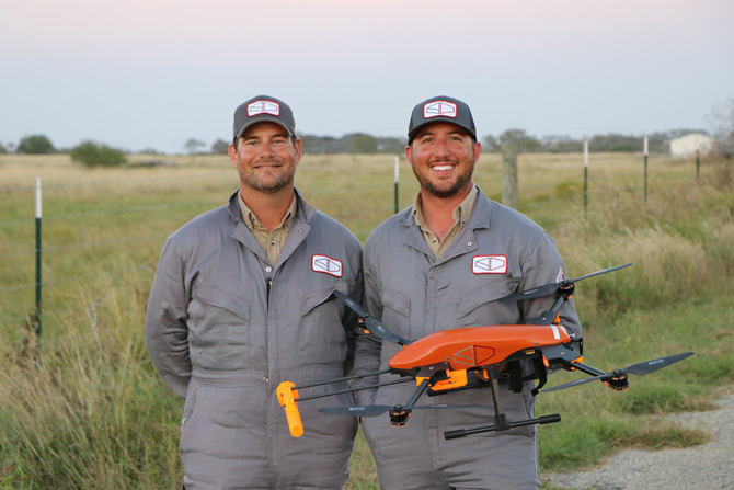 SeekOps founders in matching gray work clothes holding an orange drone outdoors